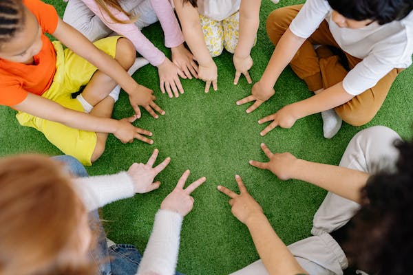 Niños sentados en circulo sobre el césped con las manos adelante