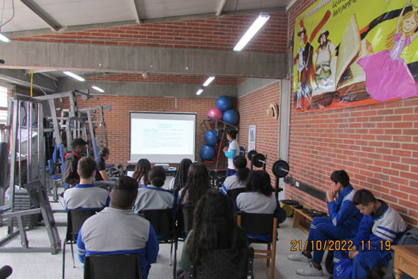 Estudiantes en el gimnasio viendo una presentación en pantalla