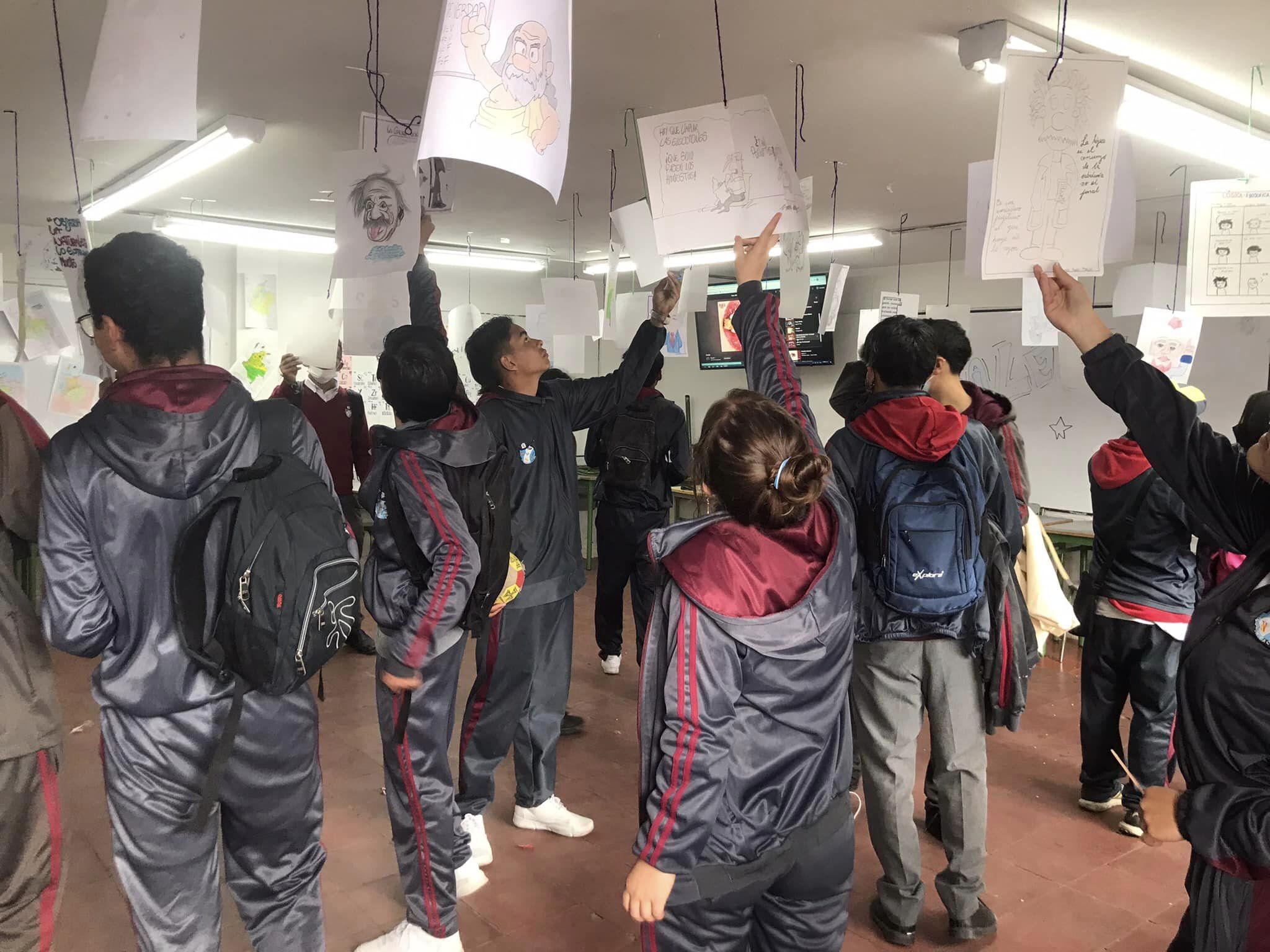 Estudiantes observando dibujos colgados desde el techo del salón