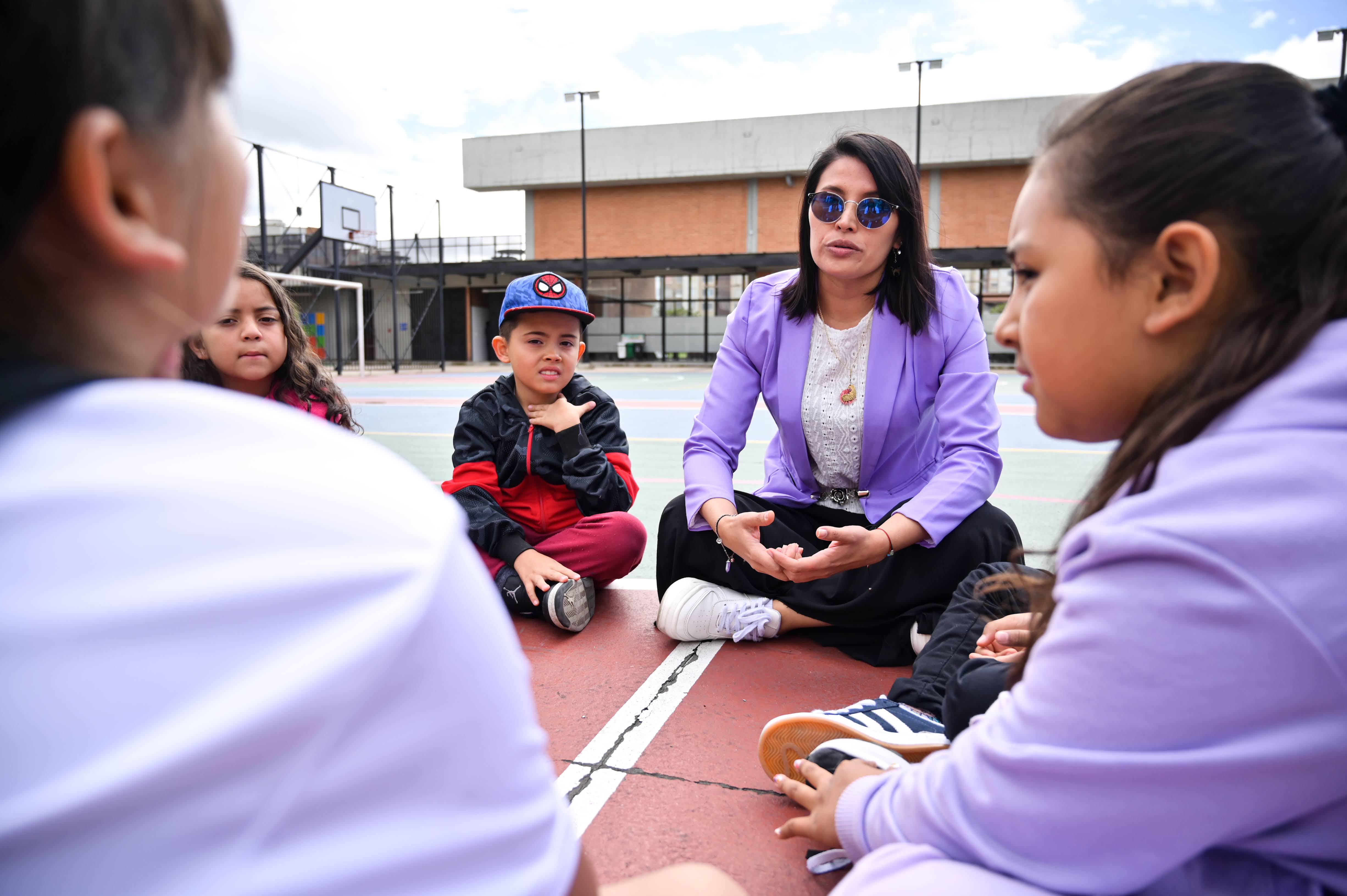 Foto de una profe hablando con sus estudiantes pequeños sentados en el suelo